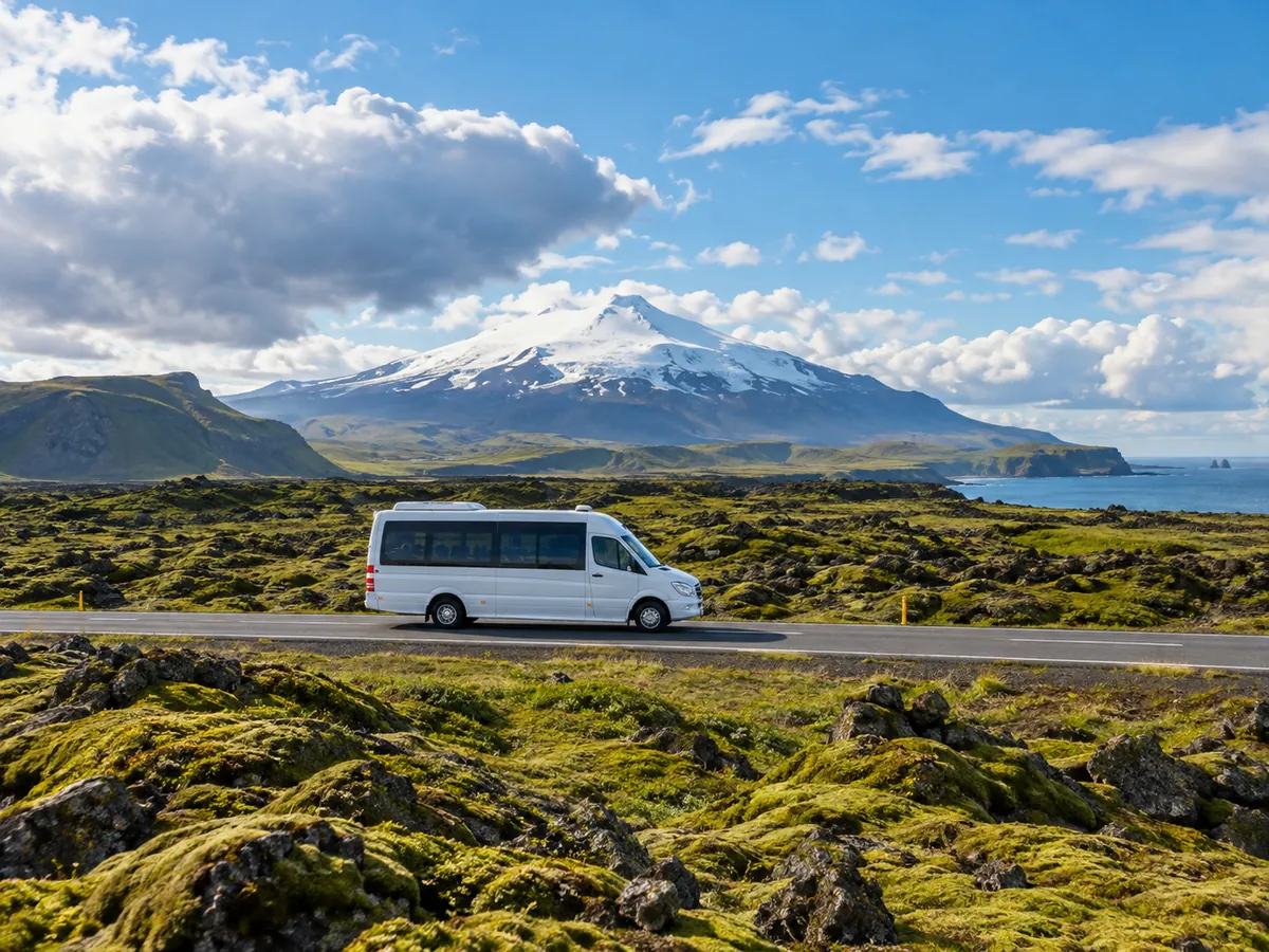 Ein weißer Minibus auf einer Straße durch moosbewachsene Lava mit dem Snaefellsjokull im Hintergrund