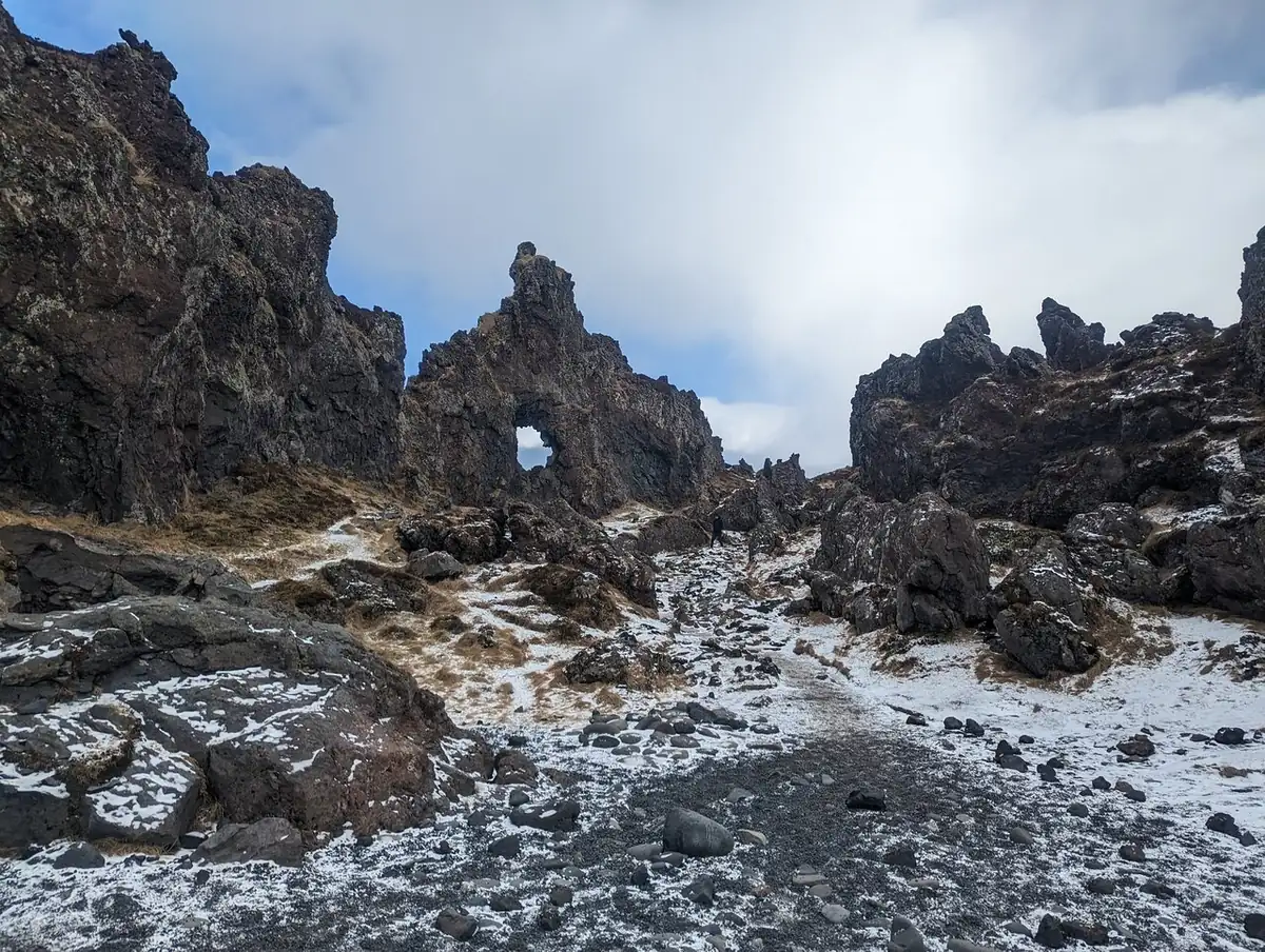 Zerklüftete Lavafelsen mit einem natürlichen, schneebestäubten Bogen bei Dritvik