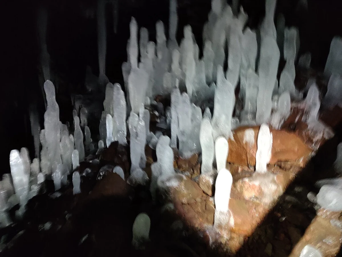 Eisformationen, die vom Boden einer dunklen Lavahöhle aufragen